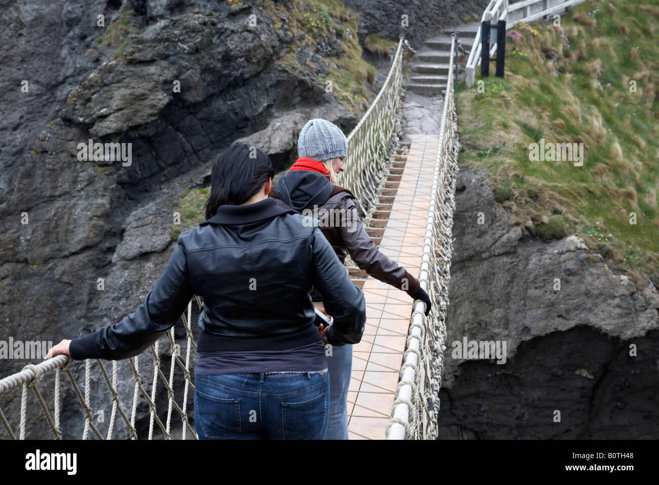 zwei weibliche Touristen zu Fuß über die Carrick eine Rede-Hängebrücke über die Grafschaft Antrim Küste Nordirland Stockfoto
