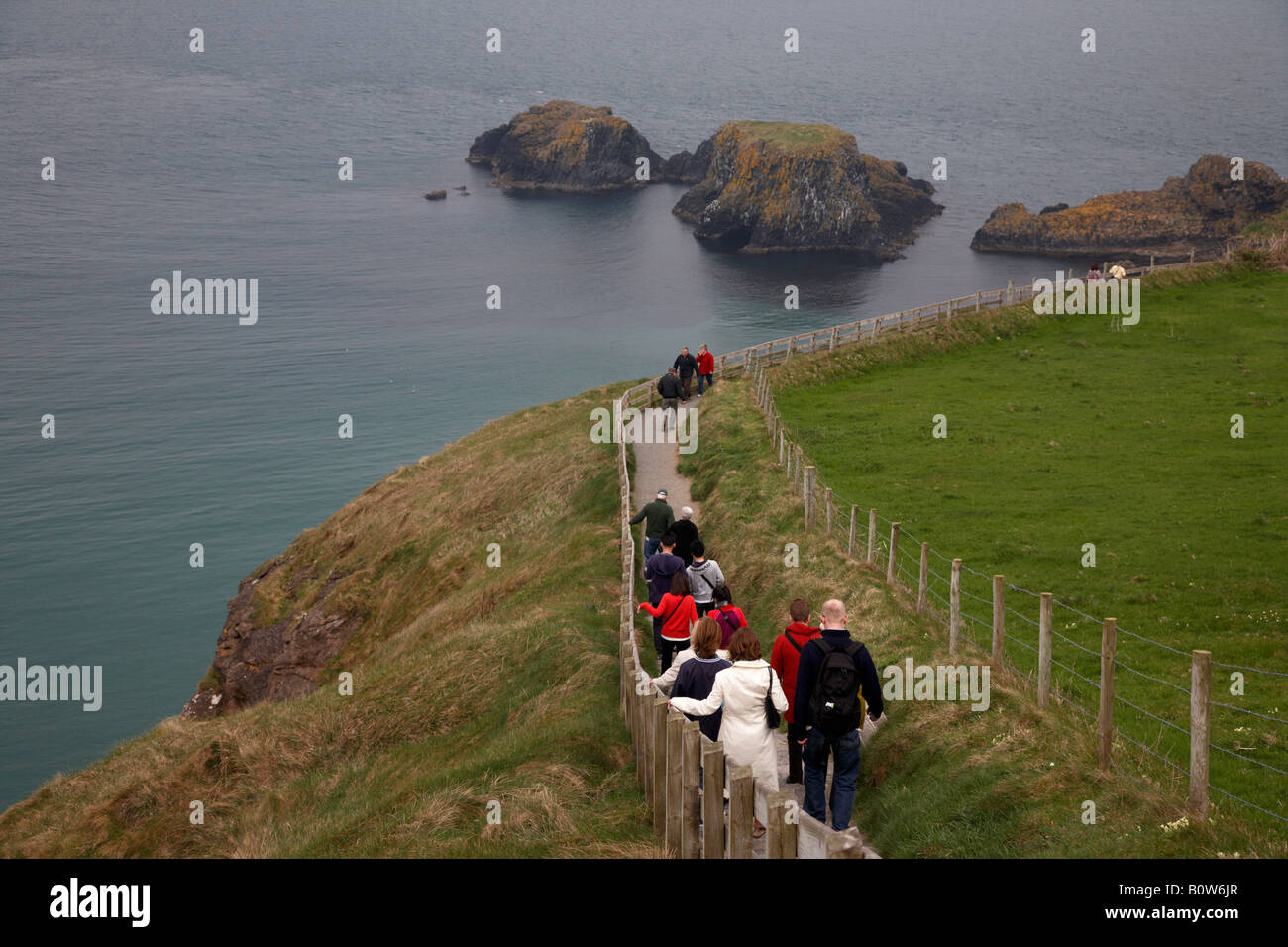 Touristen gehen den langen Weg hinunter zu den Carrick eine Rede Seilbrücke auf der Grafschaft Antrim Küste Nord-Irland Stockfoto