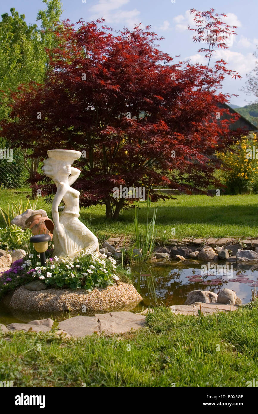 Europäischen Garten mit Teich, Statue und Pflanzen um sie herum. Stockfoto