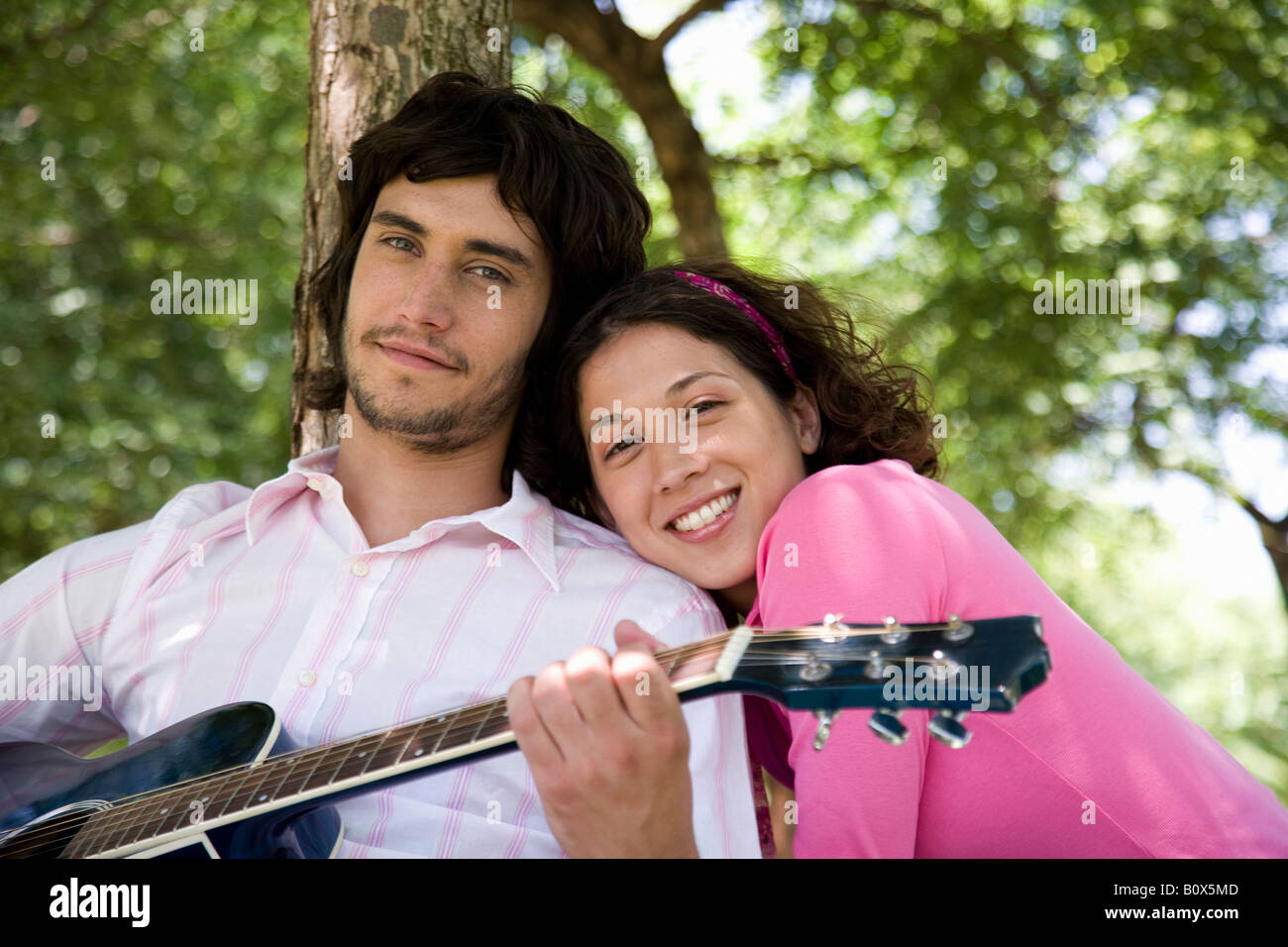 Ein junges Paar sitzt unter einem Baum und Gitarre Stockfoto