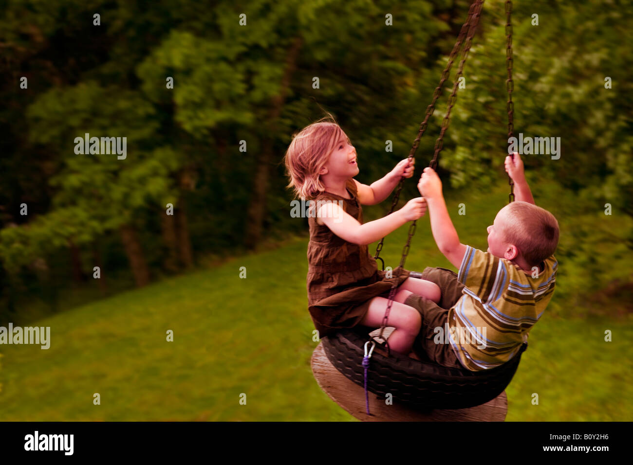 Ein kleiner Junge und ein Mädchen loslassen schwingen auf einer Reifenschaukel Stockfoto