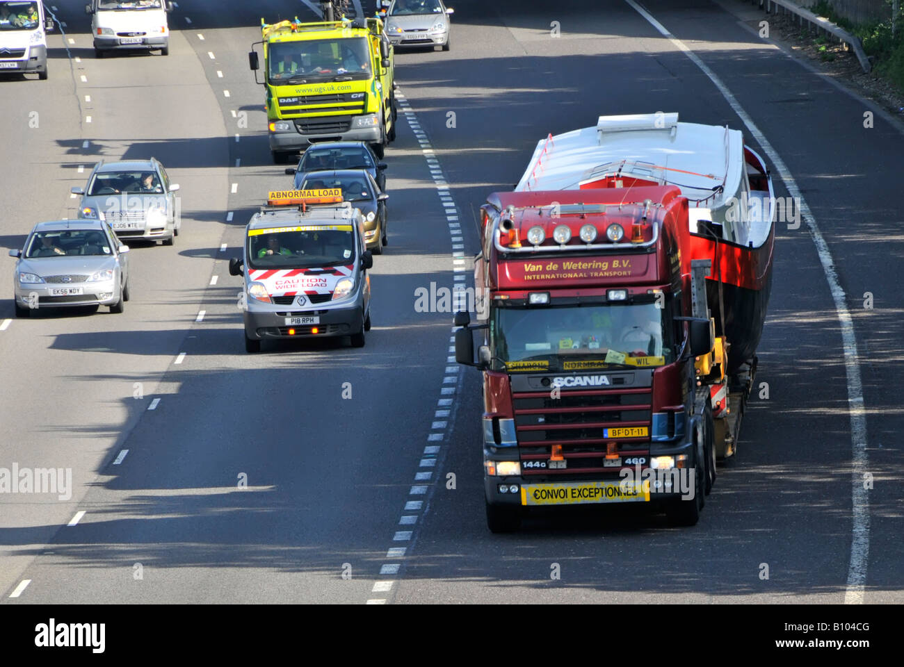 Scania LKW-Lkw fährt M25 m auf der Autobahn breite übergroße Bootsladung auf Tieflader, die auf die Autobahn-Zubringerstraße CONVOI AUSSERGEWÖHNLICHES Essex England UK trifft Stockfoto