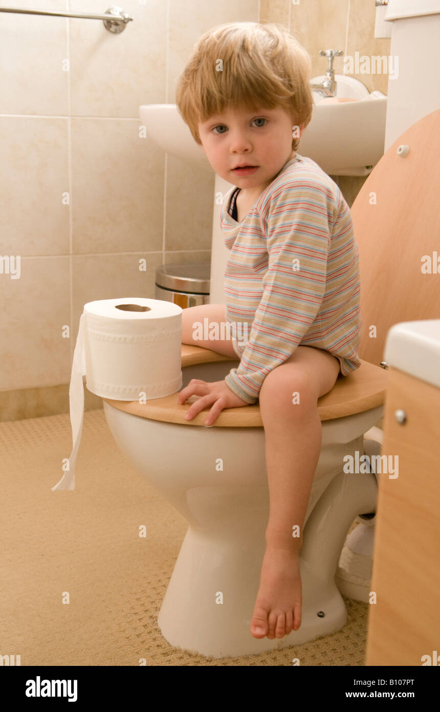 Kleines Kind, Junge, lernt, die Toilette zu benutzen, Klo, sitzt auf dem Sitz und hält eine Papierrolle, 27 Monate alt Stockfoto