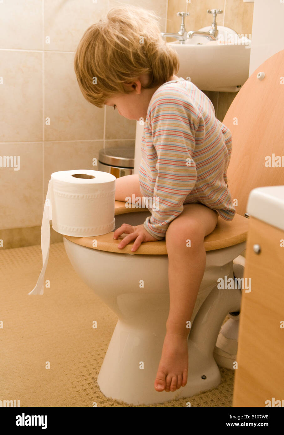Kleines Kind, Junge, lernt, die Toilette zu benutzen, Klo, sitzt auf dem Sitz und hält eine Papierrolle, 27 Monate alt Stockfoto