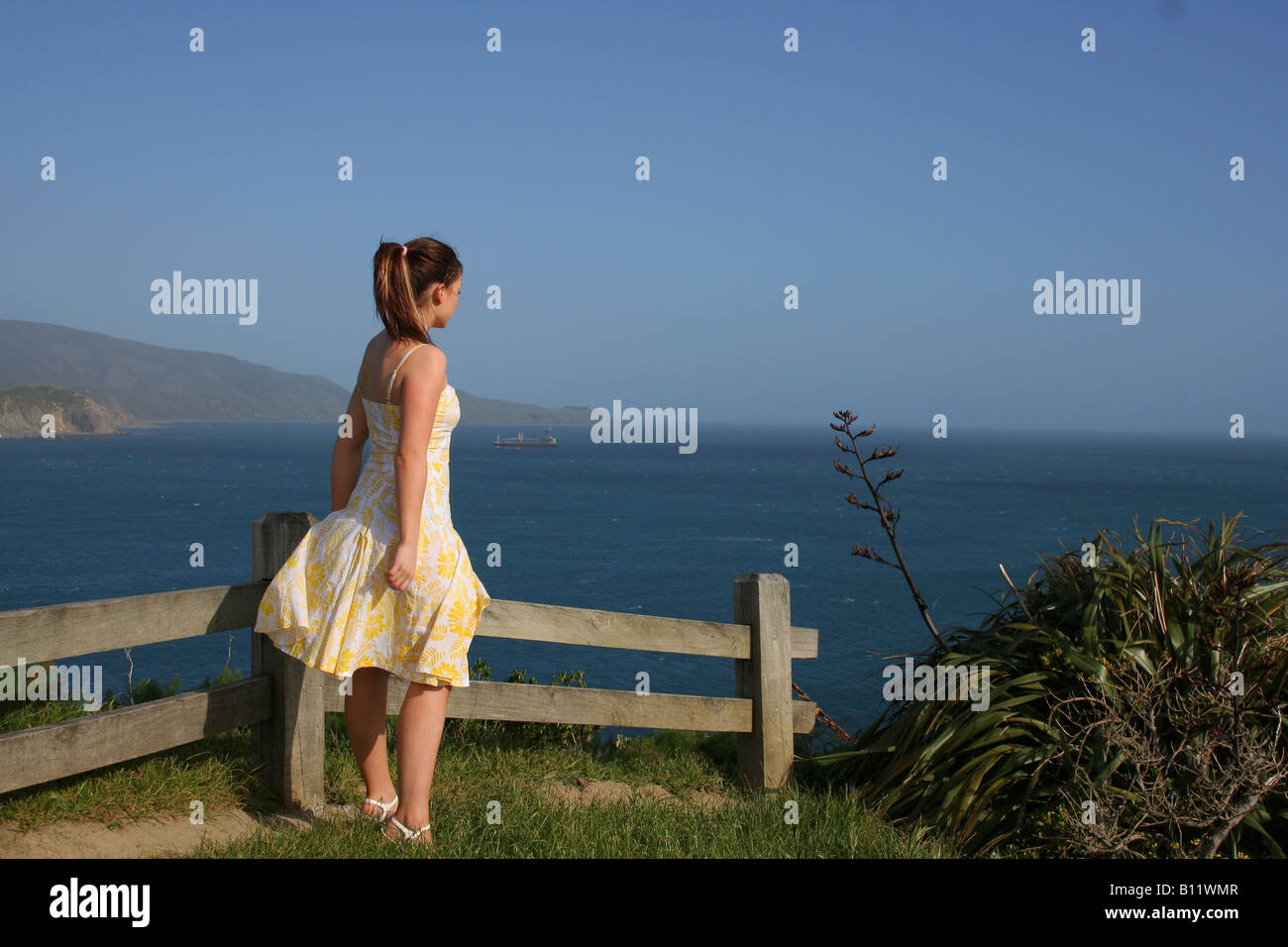 Junge Frau in einem Kleid mit Blick auf den Ozean von einem Hügel aus. Stockfoto