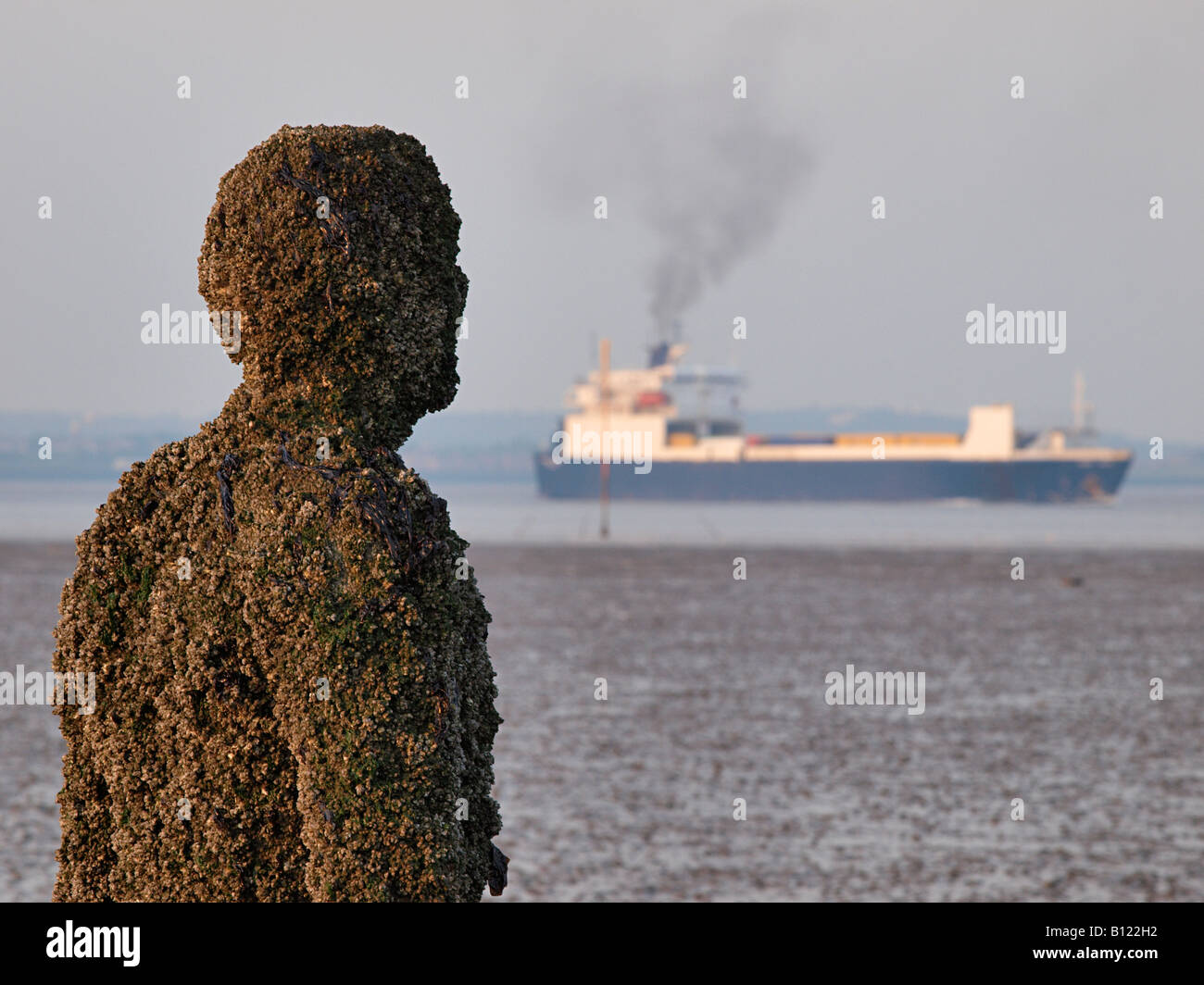Antony Gormley geschnitzte Figur am Strand mit vorbeifahrenden Schiff auf dem Fluss Mersey, Crosby, Liverpool, Merseyside, England, Vereinigtes Königreich, Stockfoto