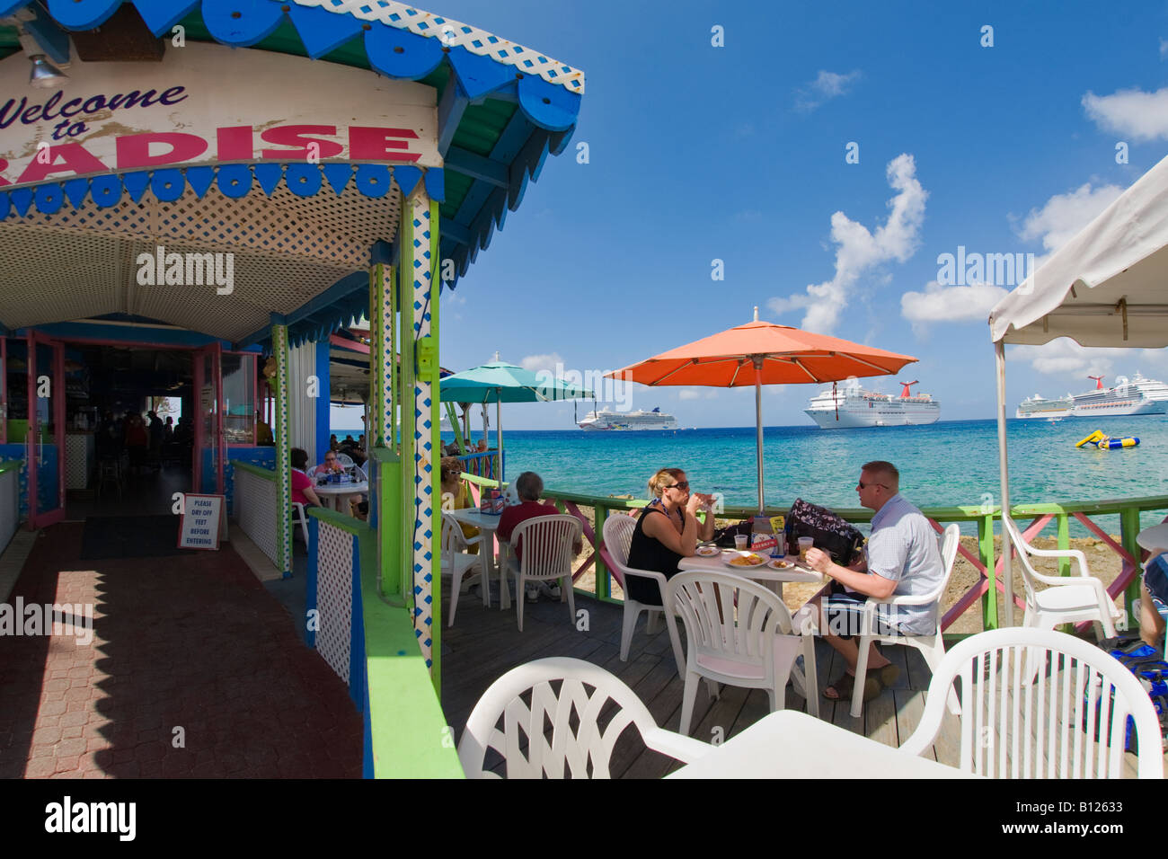 Restaurant im Freien an Georgetown Waterfront auf Grand Cayman auf den Cayman Islands in der Karibik mit Kreuzfahrtschiffen in backgrd Stockfoto