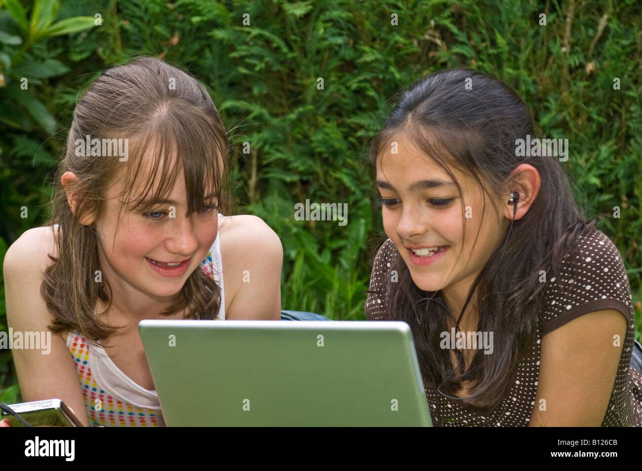 Zwei junge Mädchen (10 Jahre) die besten Freunde in den Garten, Blick auf den tragbaren Rechner mit MP3-Musik-Player und Kopfhörer auf. Stockfoto