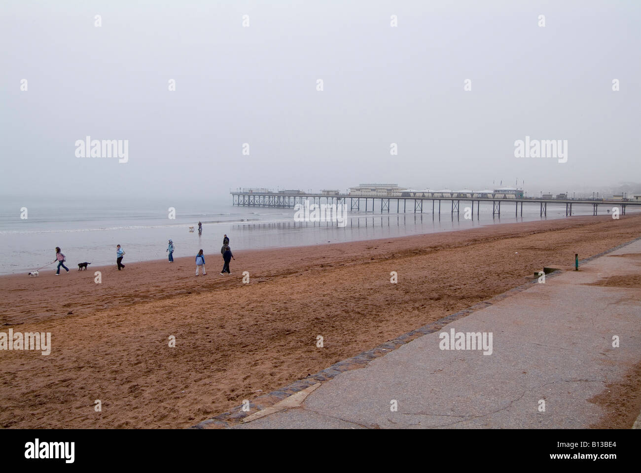Strand mit Spaziergängern und dem Pier an einem nebligen Wintertag, Paignton, Devon. VEREINIGTES KÖNIGREICH Stockfoto