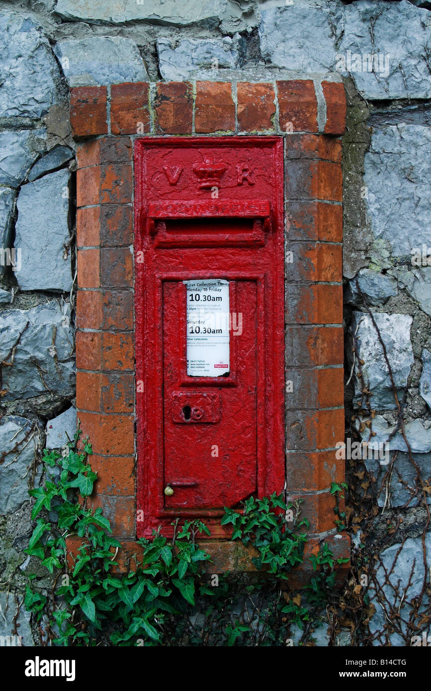 Alte rote Briefkiste mit gelber Schnecke, die auf sie klettert, in der Wand. Somerset. Stockfoto