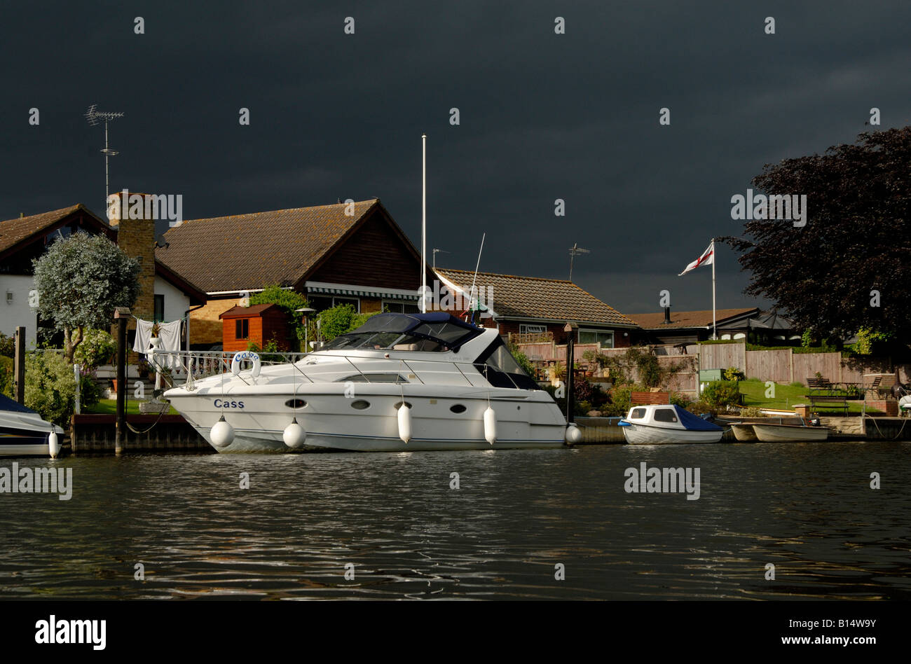 Große weiße Motoryacht vor Anker vor am Flussufer-Häusern unter schwarzen bedrohlichen Himmel, Themse, Walton on Thames, Surrey Stockfoto