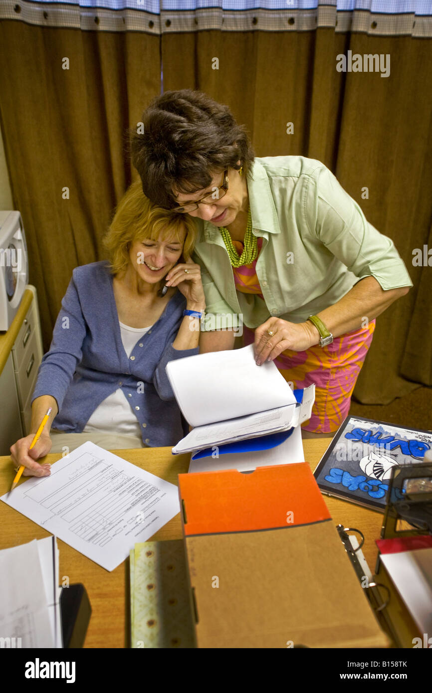 Eine Sonderschullehrerin in einer Mittelschule in Südkalifornien überprüft durch Papierkram während ihr Kollege spricht am Telefon Stockfoto