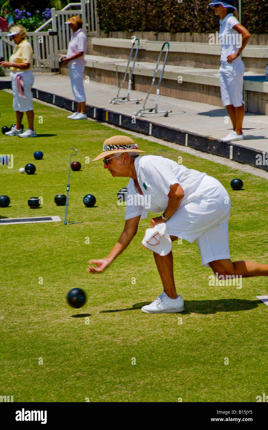 In der Verordnung weiße Uniform rollt eine Spielerin einen Schüssel Ball während einer Rasen-Bowling-Wettbewerb auf ein Bowling green Stockfoto