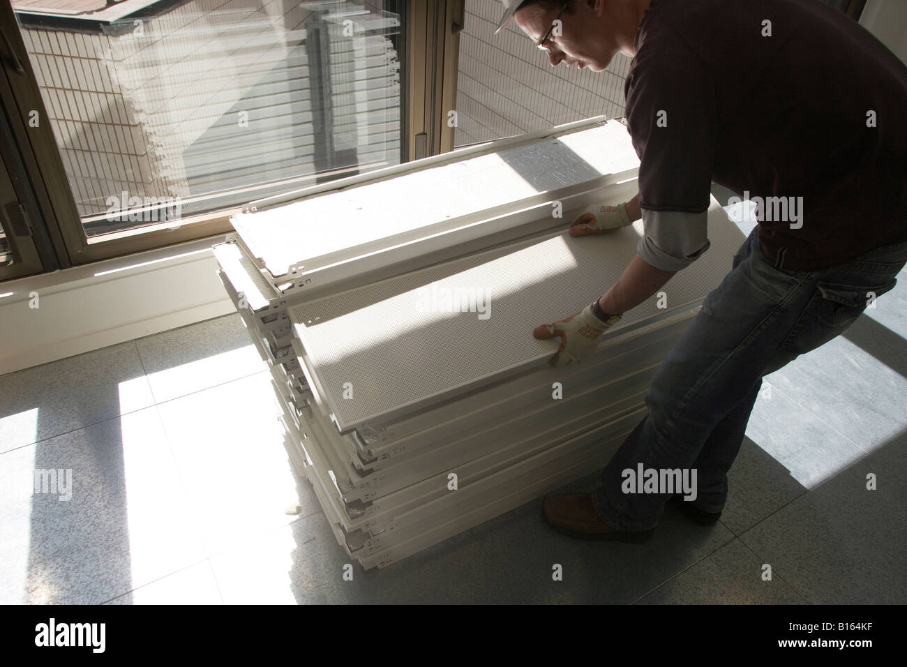 Ein Arbeiter nimmt Deckenplatten aus einem großen Stapel. Stockfoto