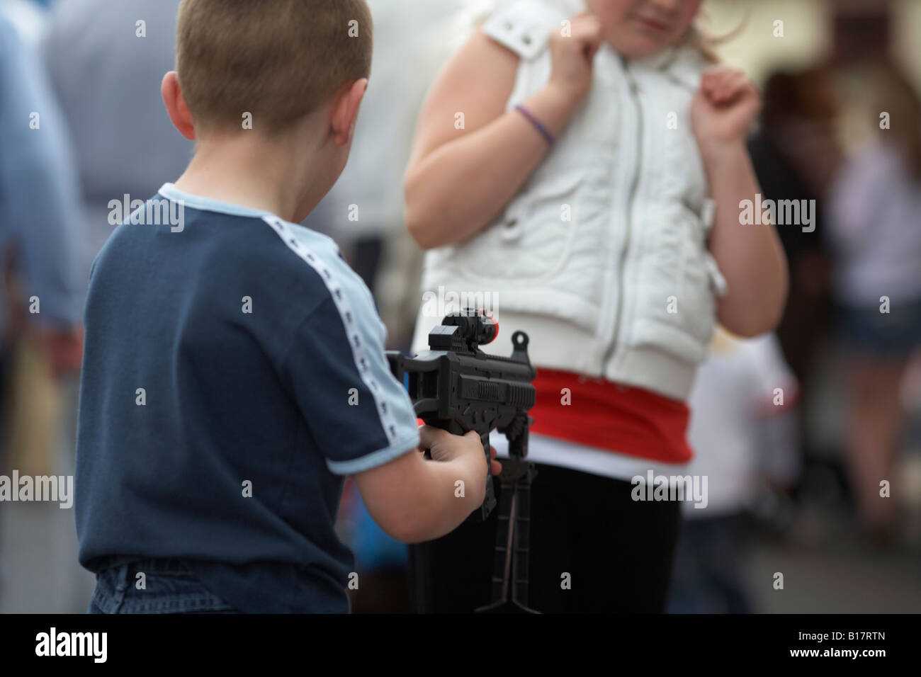 Junge mit Spielzeugpistole in bedrohlichen gegenüber Mädchen in gespielter Angst Rolltore Stockfoto
