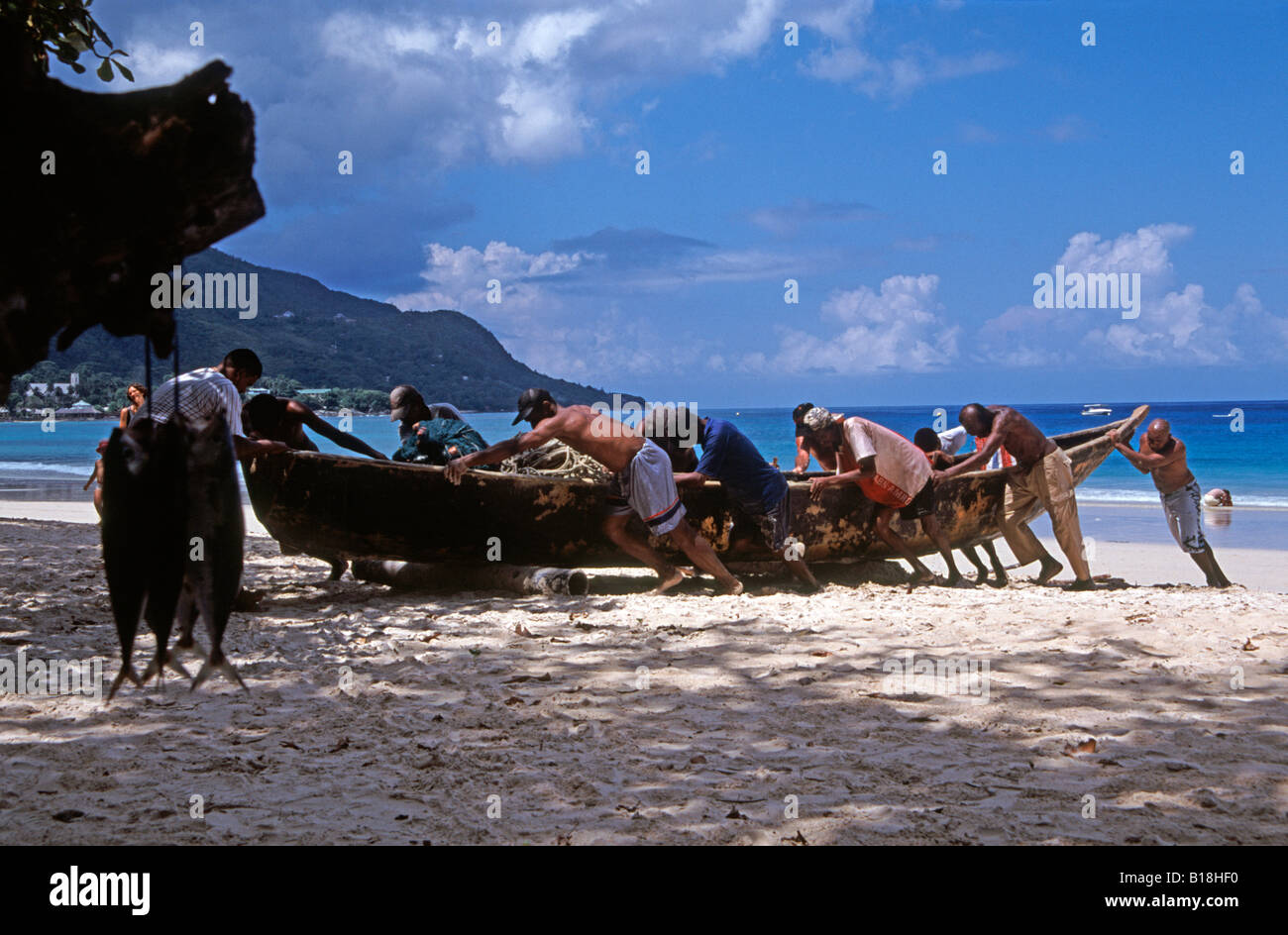 Fischer, die den Dugout am wunderschönen Strand von Beau Vallon auf Mahe, Seychellen, Indischem Ozean, anschleppen Stockfoto