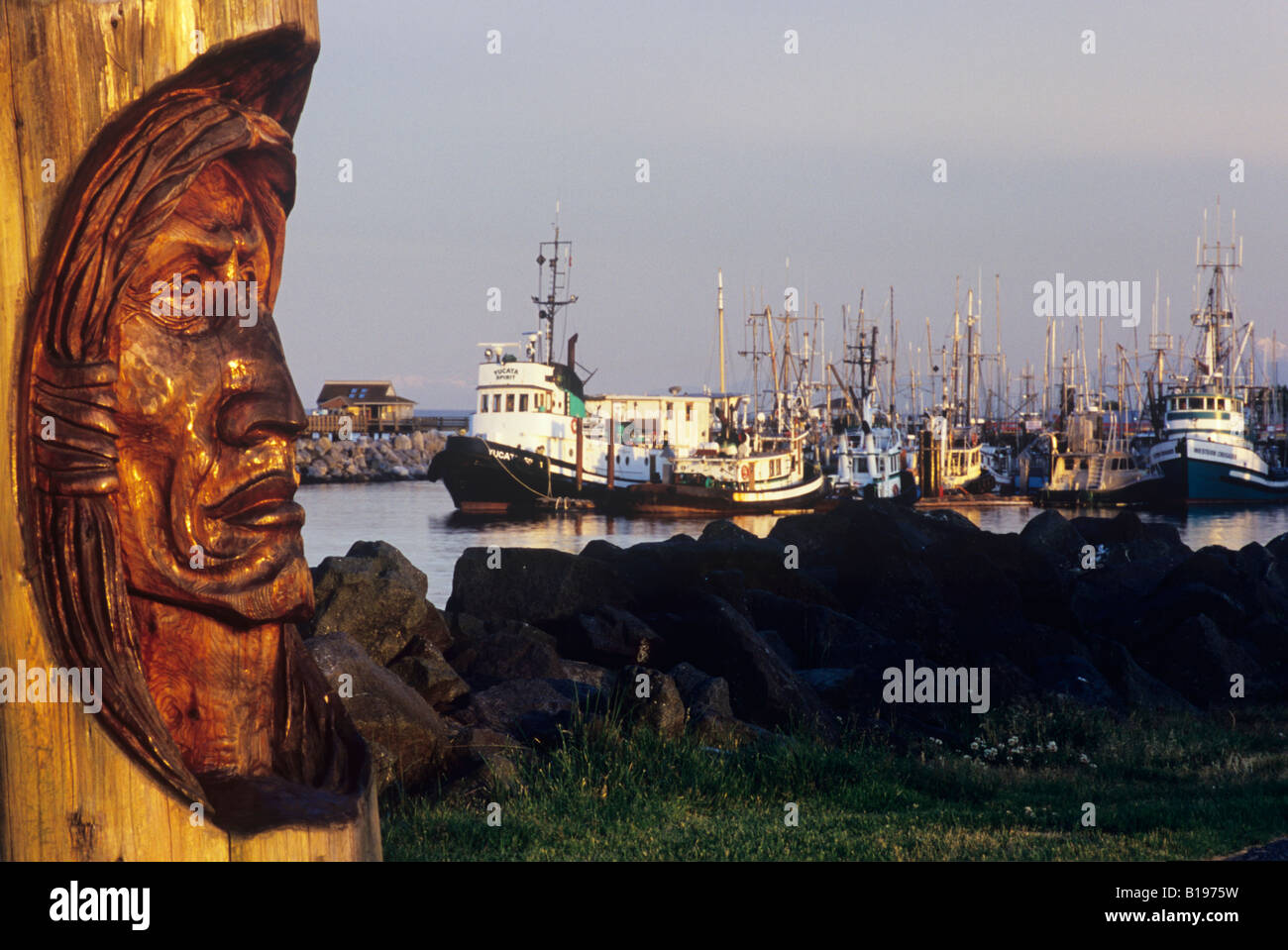 Native Gesicht geschnitzt in Holz-Block, Angeln Marina und Pier im Hintergrund, Campbell River, Vancouver Island, Britisch-Kolumbien, C Stockfoto