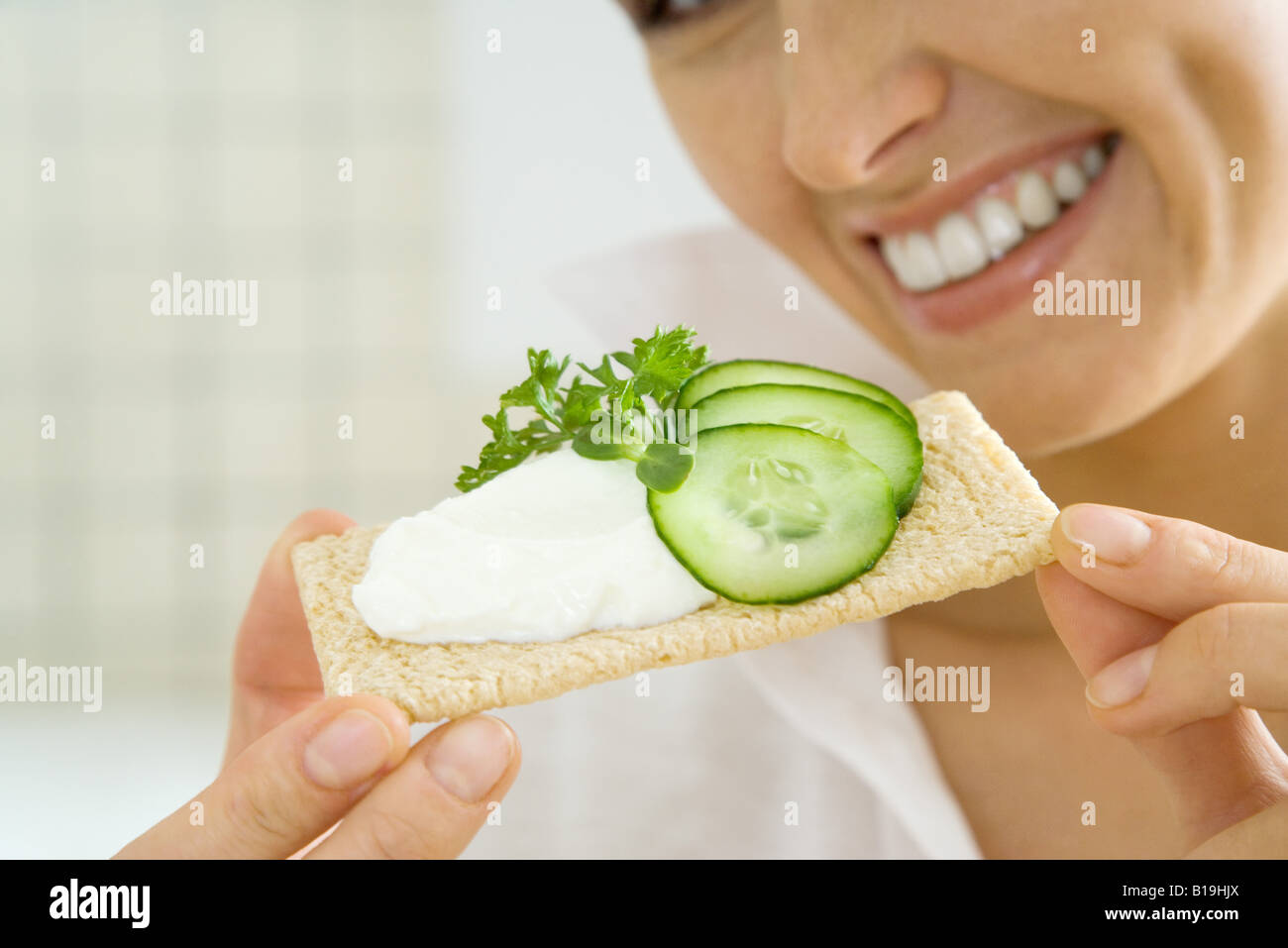 Junge Frau hält Cracker, garniert mit Gurken und Streichkäse, beschnitten Stockfoto