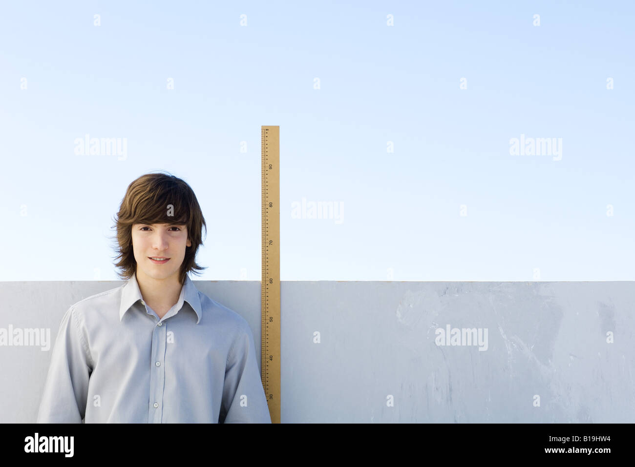Junger Mann stand neben Maßstab, lächelnd in die Kamera Stockfoto