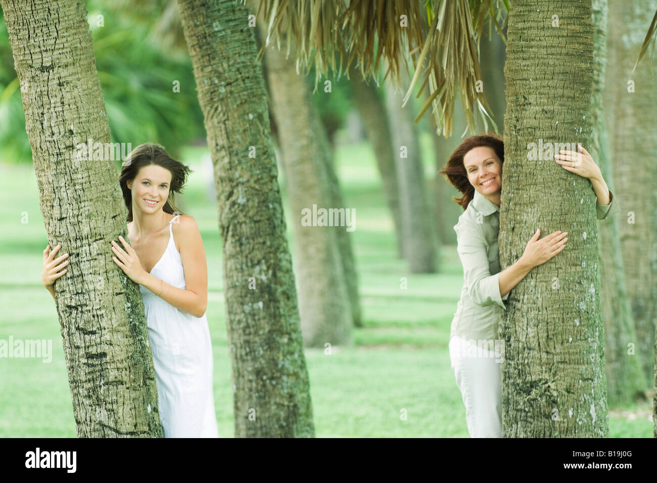 Mutter und Teen Tochter umarmt Baumstämme, lächelnd in die Kamera Stockfoto