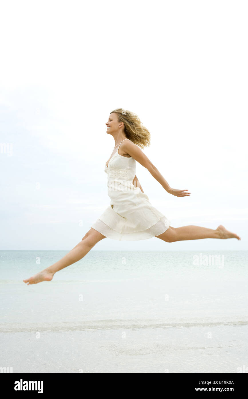 Frau springt in die Luft am Strand, Seitenansicht Stockfoto