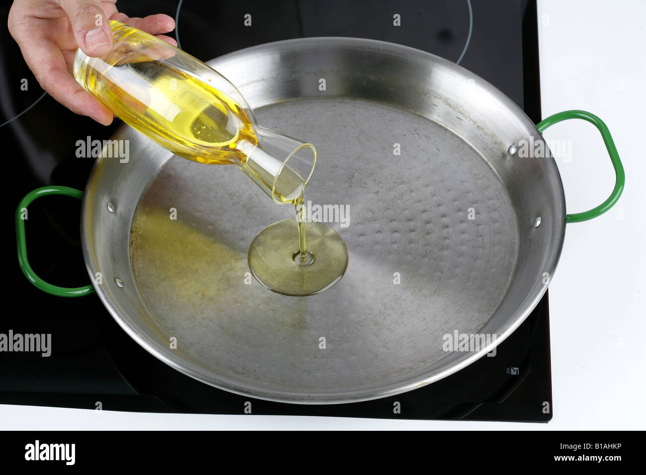 Olivenöl in der Paella-Pfanne gießen Stockfoto