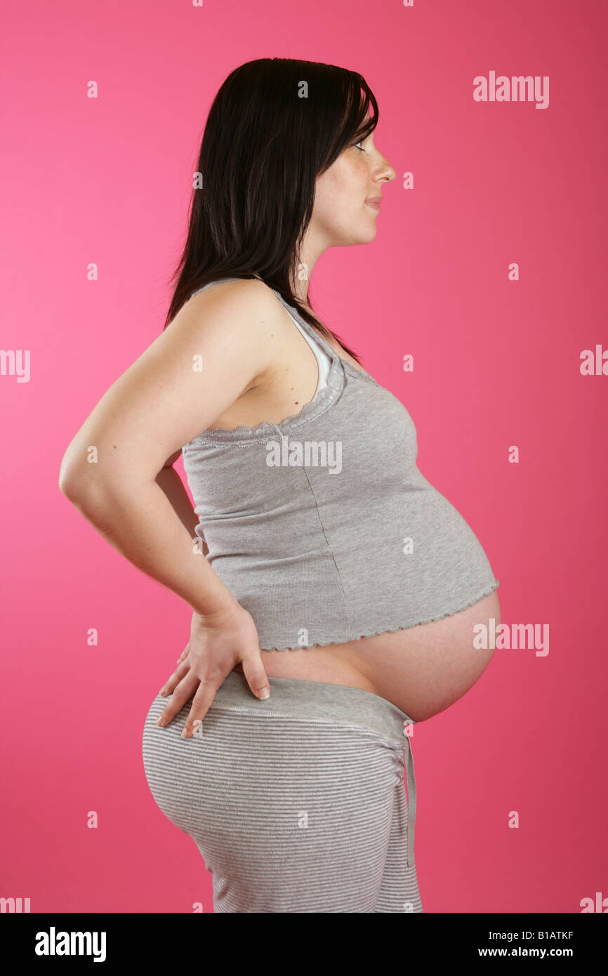 Eine Seite auf einer dunklen Haaren 38 Woche (neun Monate) schwangere Frau stehend Hand auf den Hüften tragen graue Freizeitkleidung. Stockfoto