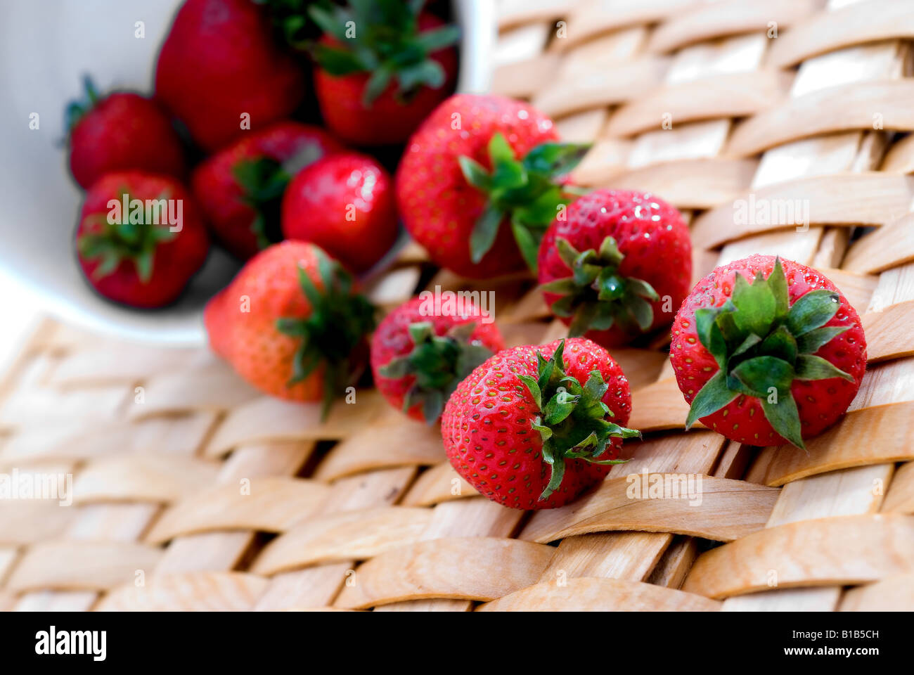 Frische Erdbeeren auf einem gewebten Teller aus einer weißen Schüssel verschütten Stockfoto