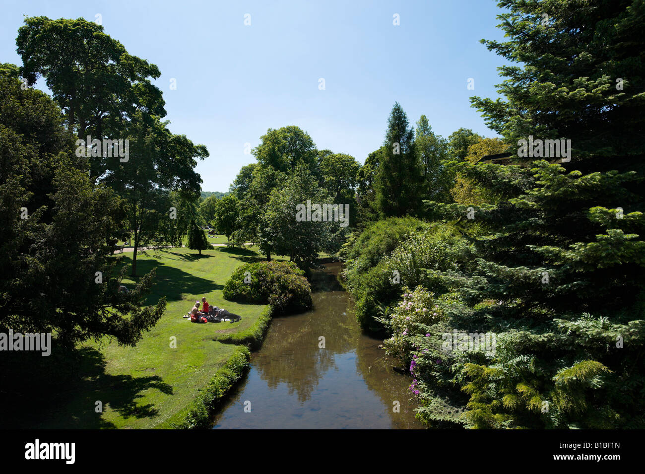 Menschen mit einem Picknick von Banken von Stream, The Pavilion Gardens, Buxton, Peak District, Derbyshire, England Stockfoto