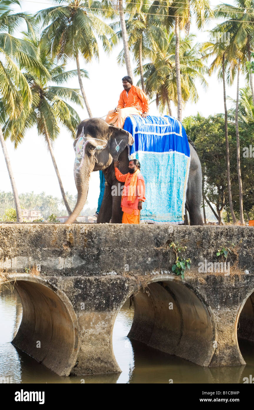 2 indischen Sadhus in Goa auf Elefanten Heiligen Religion religiöse orangefarbene Gewänder Ocker Stockfoto