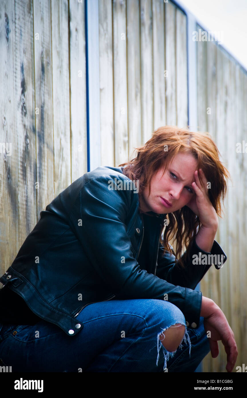 junge rothaarige rote kurzhaarige Frau Mädchen besorgt ängstlich depressiv traurig allein einsam kauerte hinunter tragen Leder Jacke im freien Stockfoto