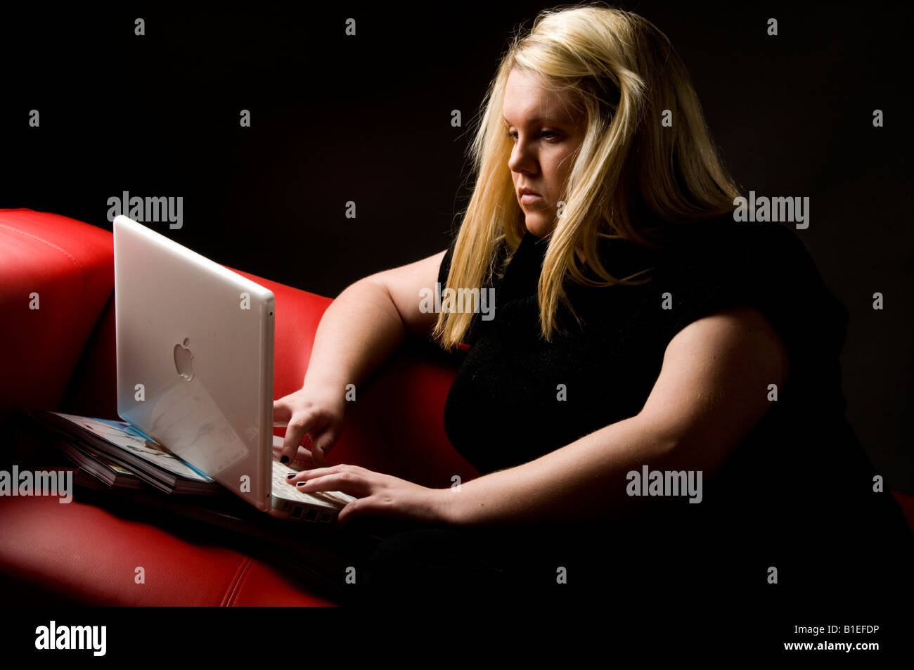 blonde junge Frau, die Arbeit an ihrem weißen Apple Mac iBook-Laptop-Computer sitzt auf einem roten Sofa, das Abrufen von e-Mails über internet Stockfoto