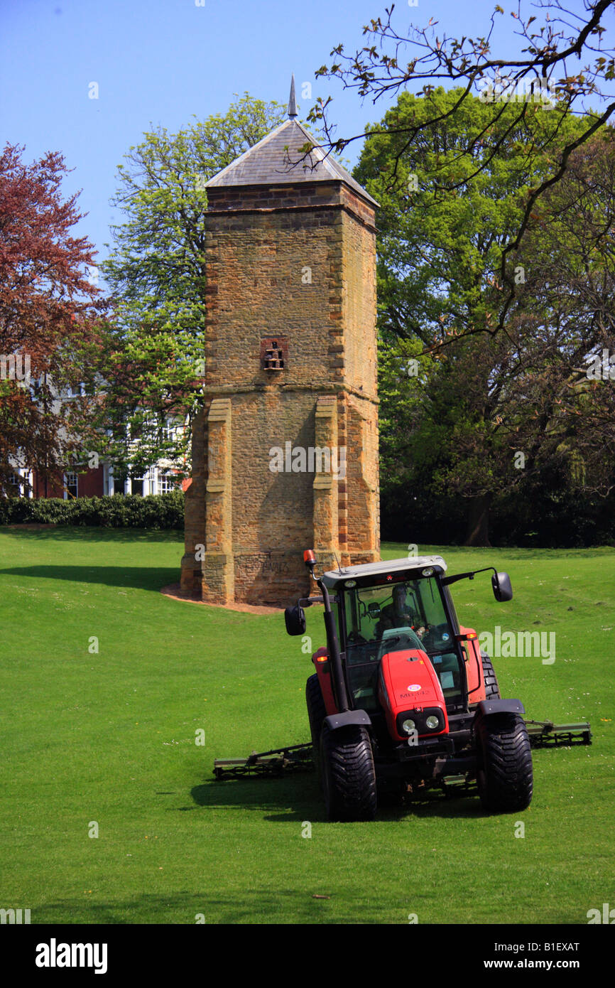 Roter Traktor Rasenmähen Parklandschaft mit uralten Turm im Hintergrund Stockfoto