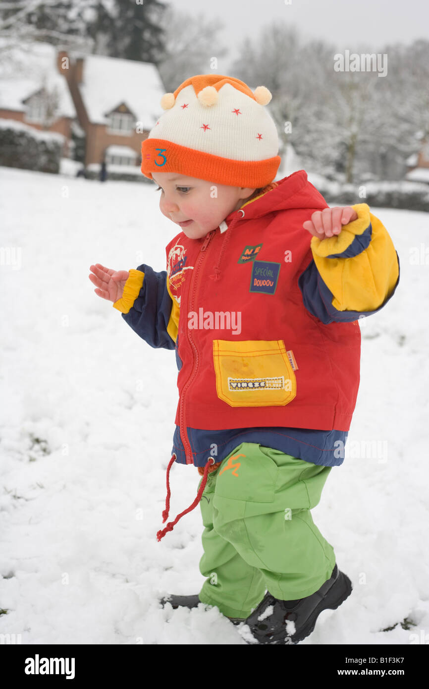 Baby in bunten Winterkleidung auf verschneiten weißen Hintergrund Stockfoto