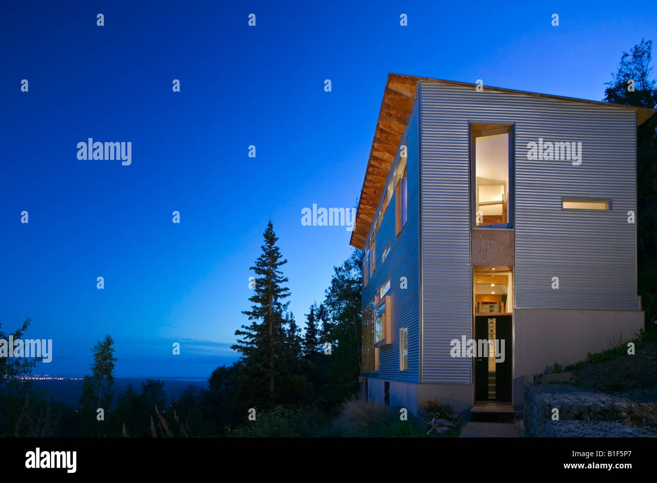 Außen von einem Handwerker Arthaus in der Dämmerung in einem bewaldeten Gebiet & Stadt Lichter im Hintergrund in Eagle River, Alaska, USA. Stockfoto