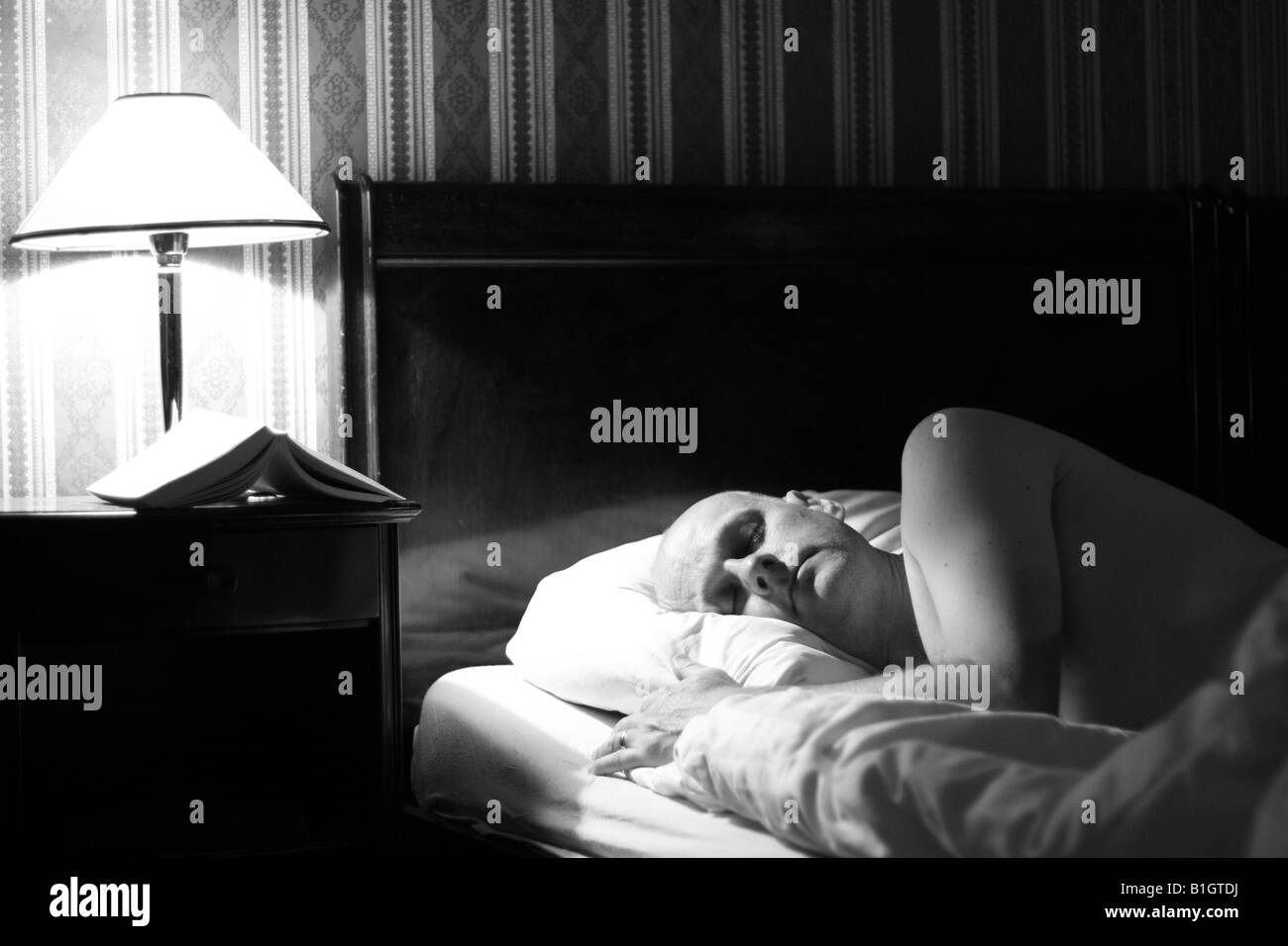 Mann im Alter von 40 Jahren schlafen im Hotel Bett Schlafzimmer mit Leselicht auf und Buch auf dem Nachttisch Stockfoto
