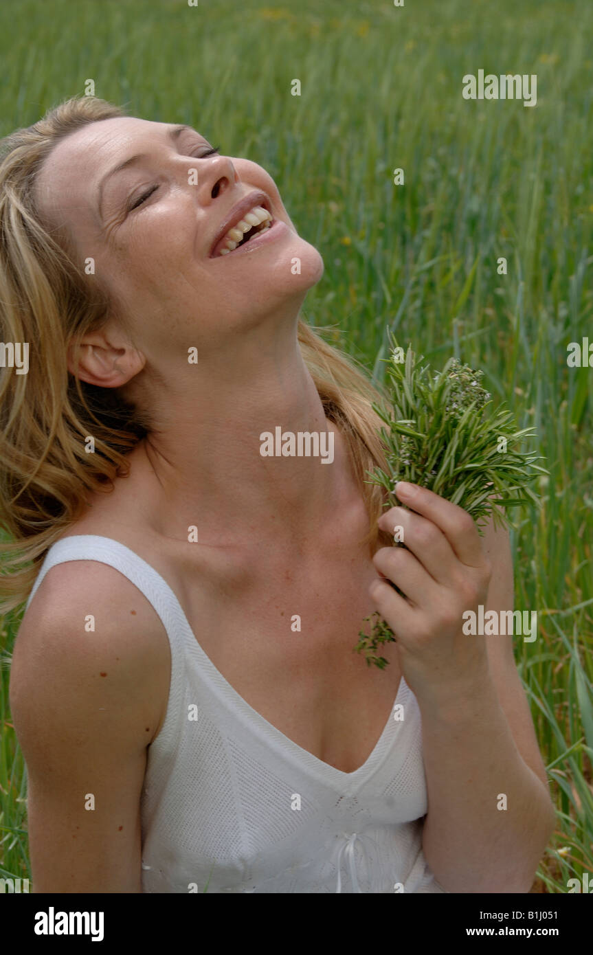 Weiß gekleidete Frauen mit einem Bouquet von Kräutern sitzt auf einer Wiese Stockfoto