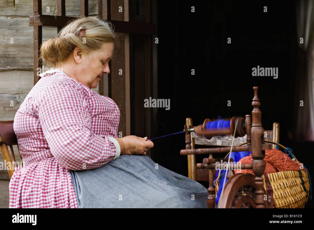 Ältere Frau in historischen Kostümen auf Veranda Kabine Spinnen Wolle in Pioneer Village im Frühjahr Mill State Park Stockfoto