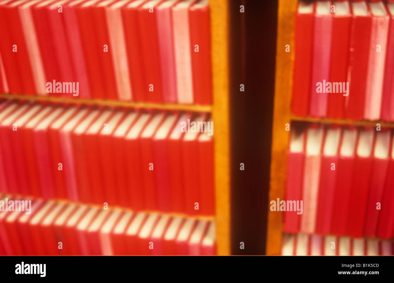 Impressionistische Reihen von nahezu identische roter Text oder Hymne oder Gebetsbücher in zwei Bücherregale in warmes Licht Stockfoto