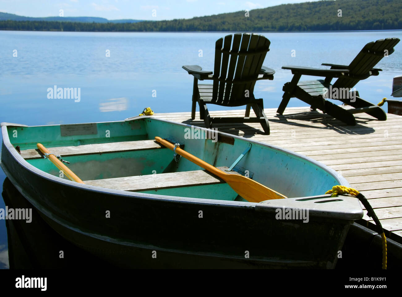 Paddelboot und zwei Adirondack Holzstühle auf dock mit Blick auf einen blauen See Stockfoto