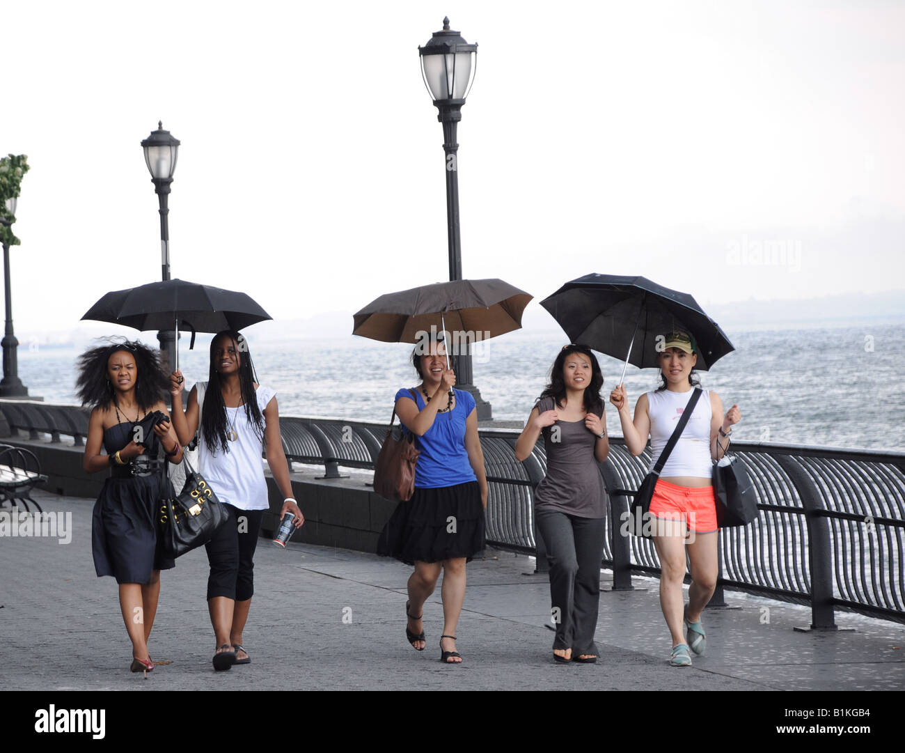 Fünf junge Frauen Fuß entlang der Battery Park City Esplanade im Regen. Stockfoto