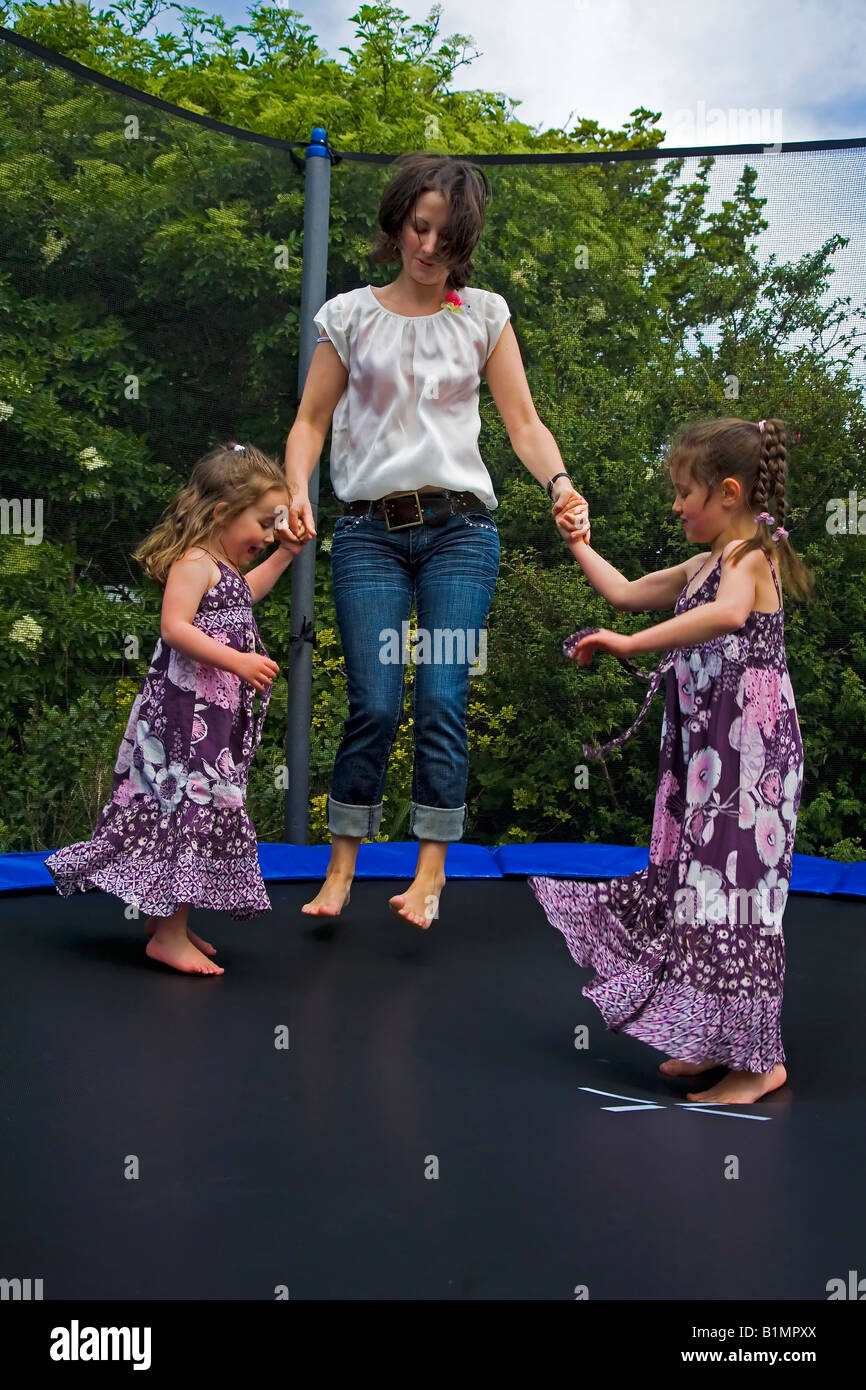 Junge Mutter und ihre zwei Töchter-Trampolin im Garten in Irland Stockfoto