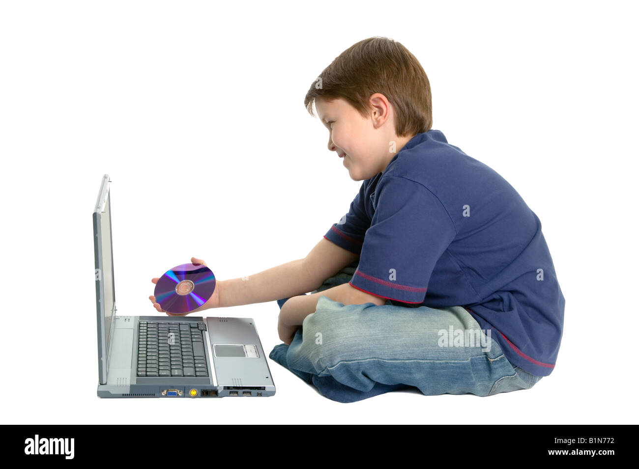 Glückliche Junge saß über Beinen in einen Laptop auf weißem Hintergrund auf eine DVD einlegen Stockfoto