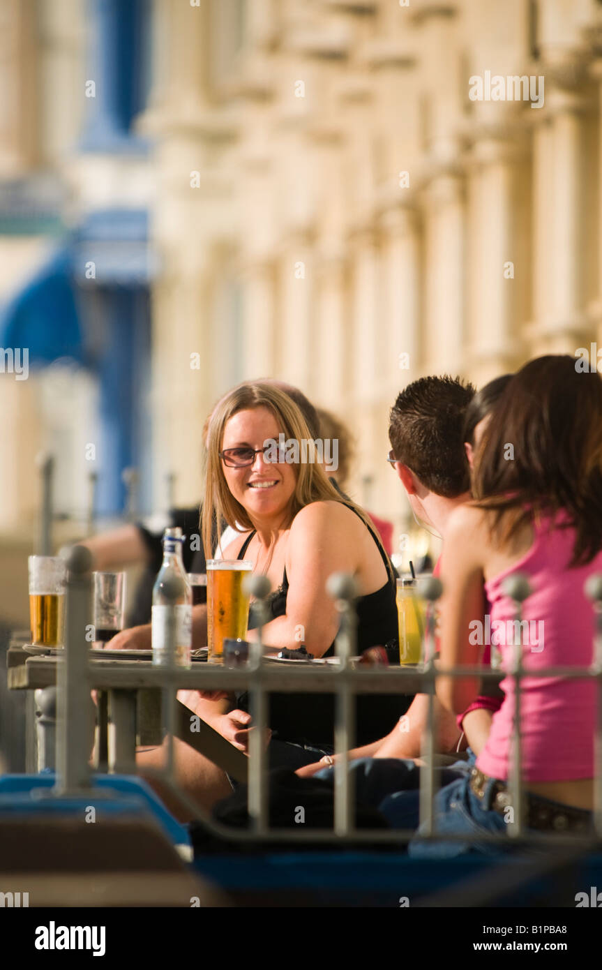 Junge, lächelnde Frau und andere Leute draußen sitzen, bar Pub Café in der Sonne trinken Bier, Aberystwyth Wales UK Stockfoto