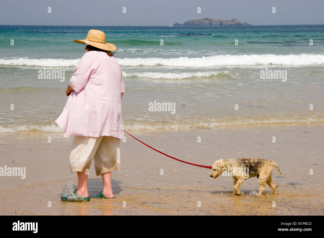 Reife Frau trägt einen Hut und ihrer sehr alten Hund entlang des Strandes an der Harlyn Bay Cornwall in England Stockfoto