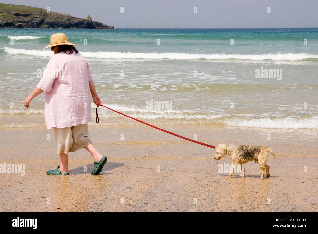 Reife Frau trägt einen Hut und ihrer sehr alten Hund entlang des Strandes an der Harlyn Bay Cornwall in England Stockfoto
