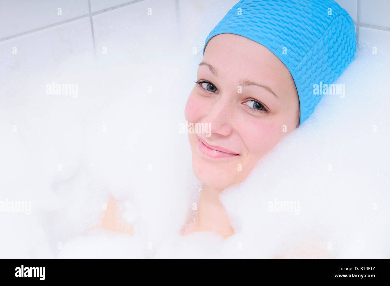 Hübsche junge Frau unter Bad in der Badewanne und entspannend, Badekappe blau Stockfotografie