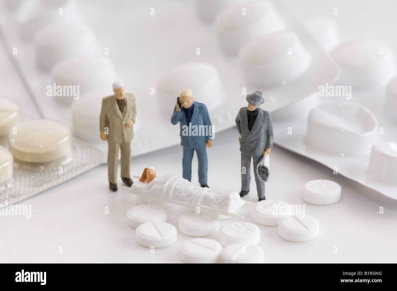 Tabletten, Blisterverpackungen und drei Miniatur-Männer stehen neben einer Frau auf einer Bahre, symbolische Foto Stockfoto