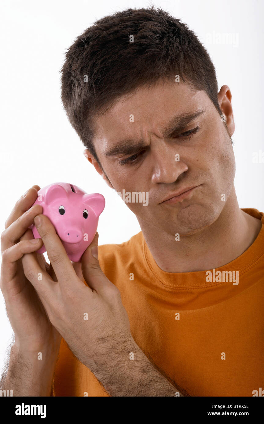 Unbekannter Mann hält ein Sparschwein an seinem Ohr Stockfoto