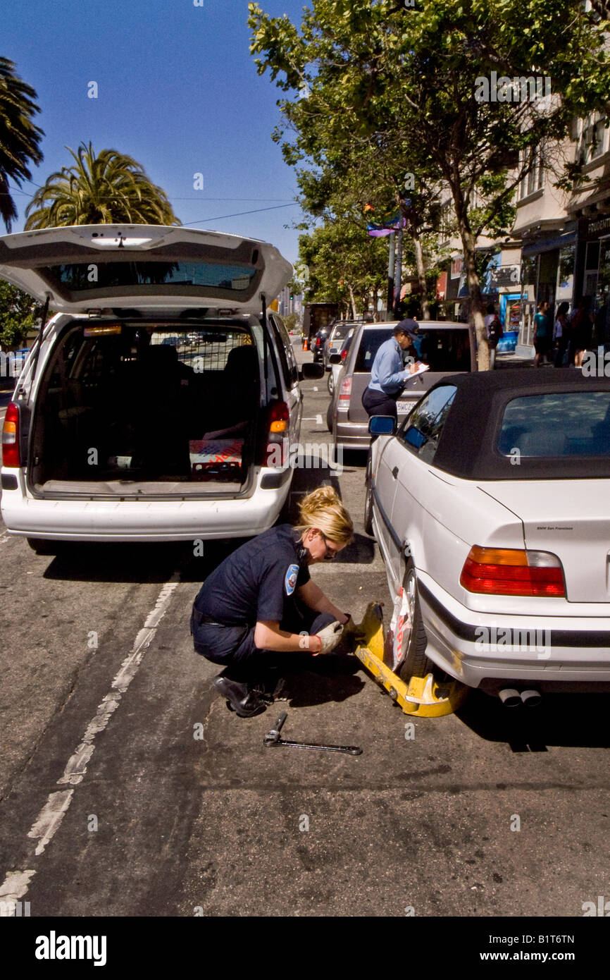 Ein Parkplatz Vollzugsbeamten installiert ein Rad Wegfahrsperre oder Boot auf ein Auto mit hervorragenden Parkplatz Verletzungen in San Francisco Stockfoto